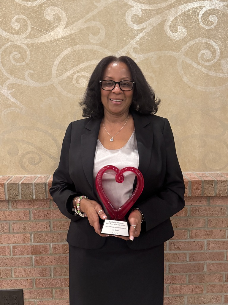 A woman smiling, standing with an award that is in the shape of a heart