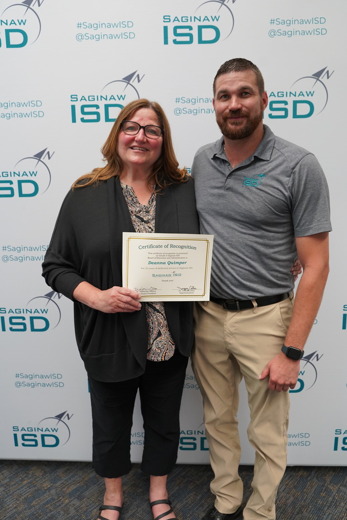 Woman and man standing with a certificate. They are standing in front of a white banner with black letters.