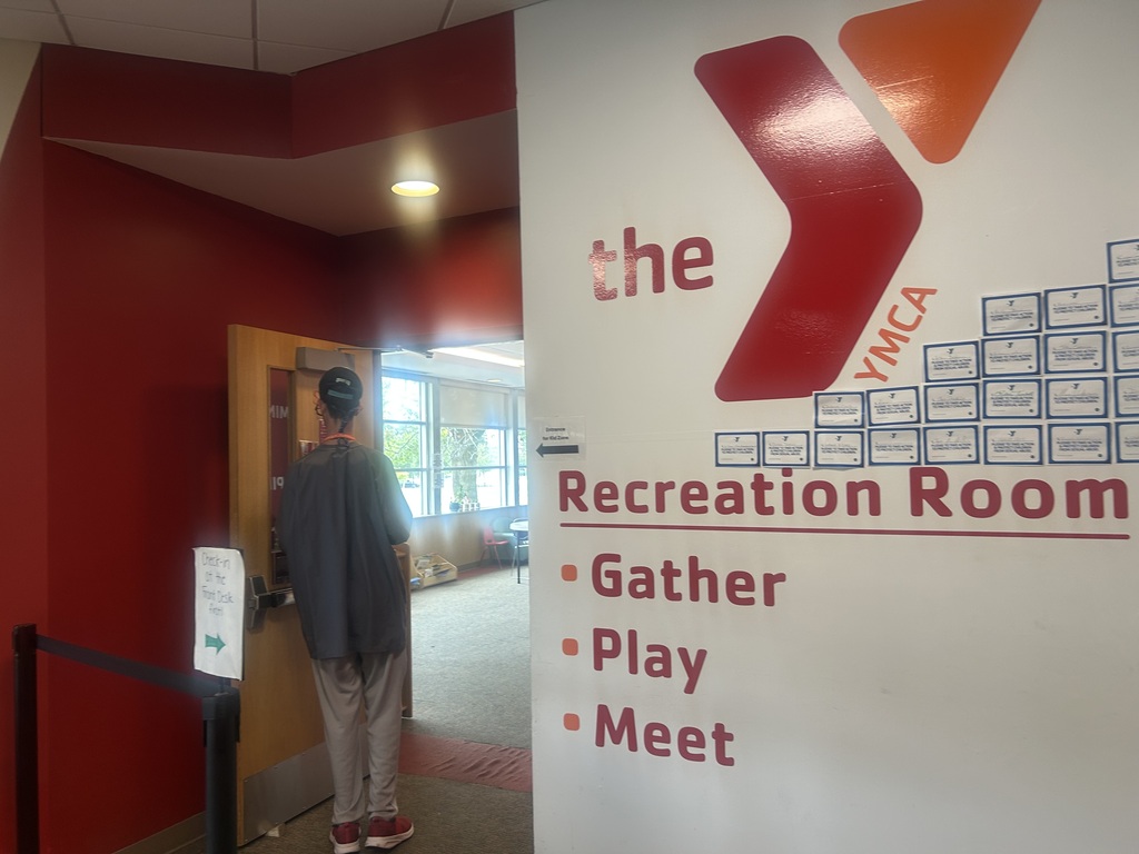A person stands at the entrance of the YMCA Recreation Room, which has a red wall and a white sign.