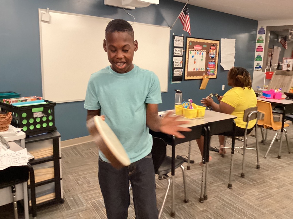 Students  play with a hand drum and tambourine during music class