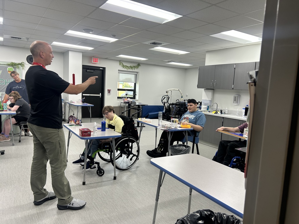 A man teaching in a classroom with students; two students in wheelchairs and others seated at desks.