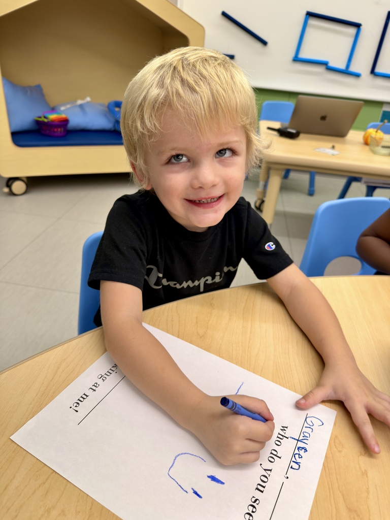 A boy wearing a black shirt with text sits at a table and draws a face.