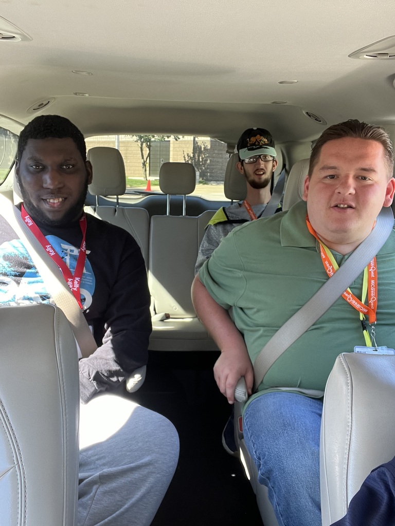 Three men in a vehicle. One wears a green shirt, another in black, and the third in gray.