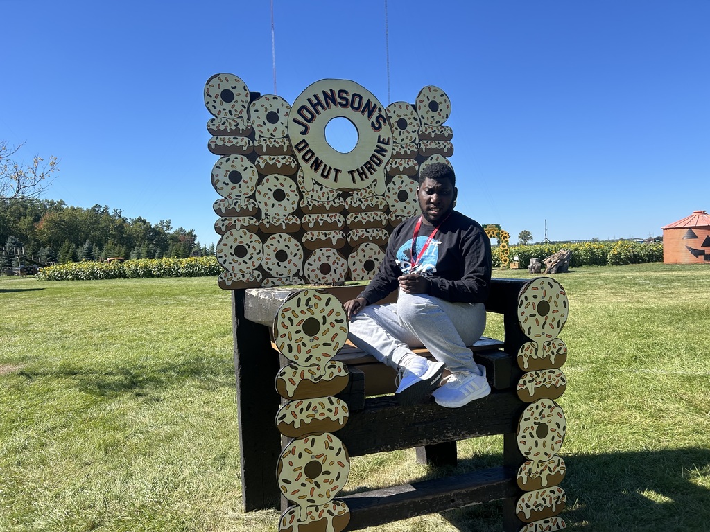 Person seated in a chair designed with donut shapes, in a field with green grass and trees.