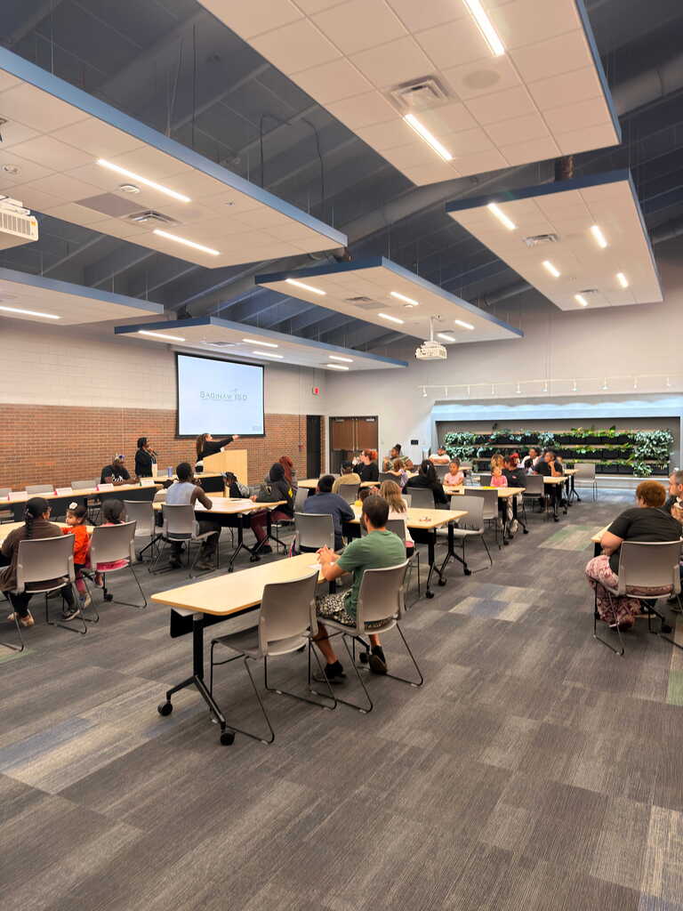 An empty classroom with chairs and tables. A projector screen is mounted on the wall.