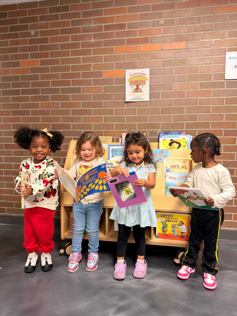 Five children in a room with a brick wall and bookshelves, holding books and looking at the camera.