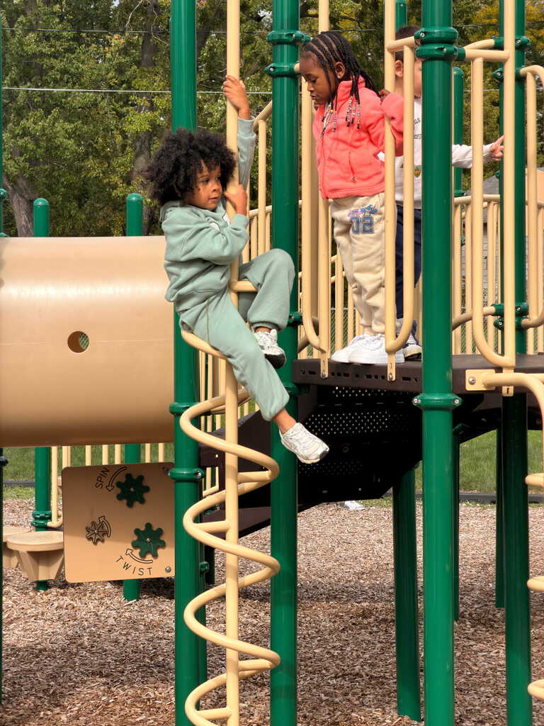 Two children in a playground, one climbing a spiral slide and another standing nearby on a platform.