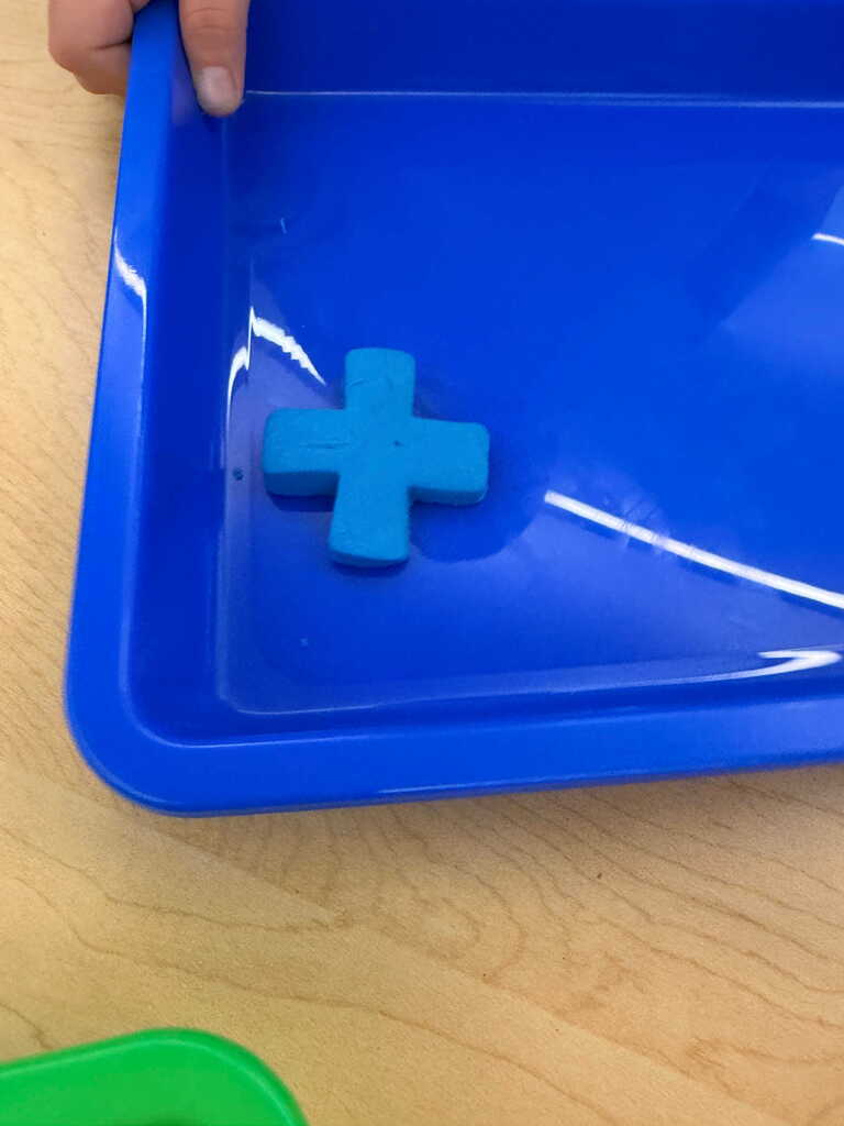 A person holding a blue tray with a blue cross in water, set on a wooden table.