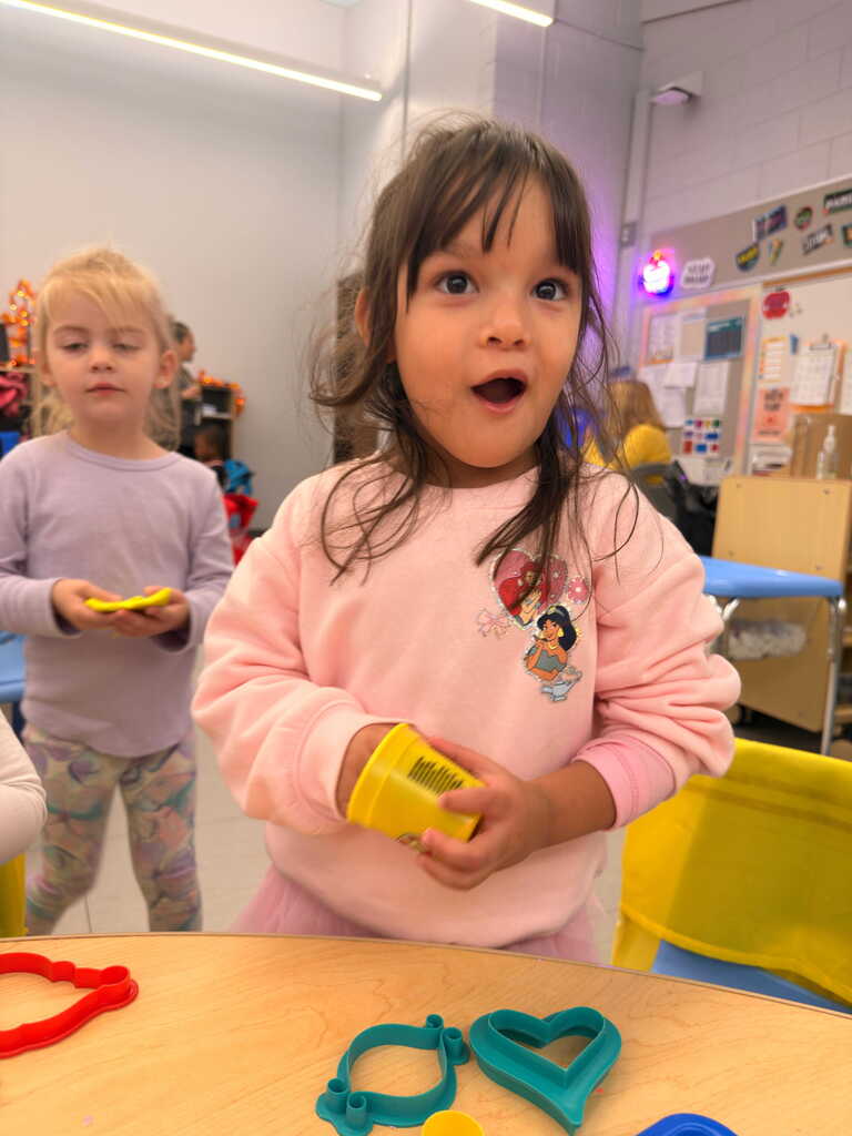 Two girls in a room. One girl holds yellow plastic shapes and makes an excited face.