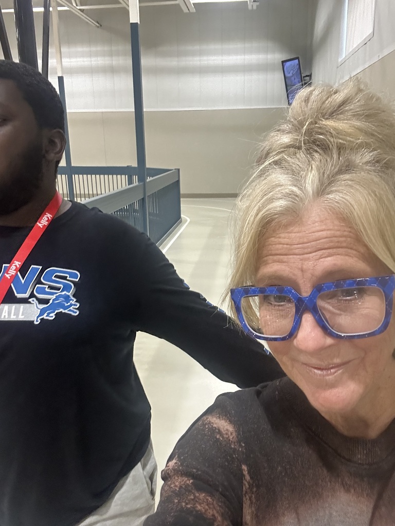 A man and woman standing, with the man wearing a Detroit Lions shirt and the woman wearing blue glasses.