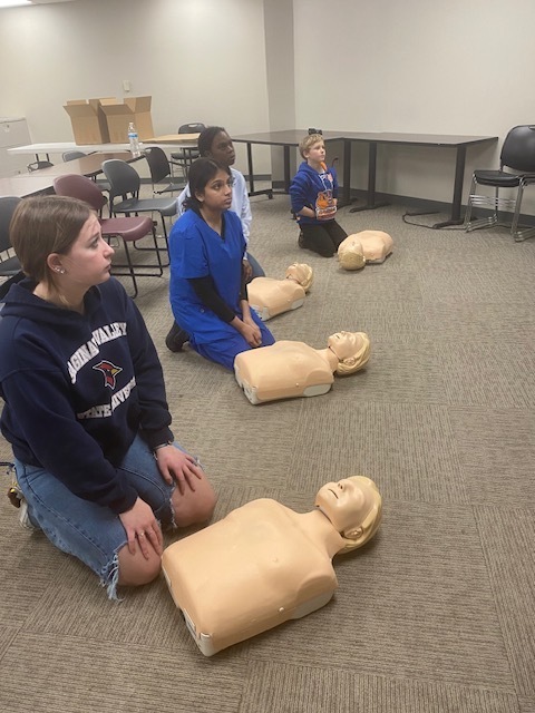 4 students in the ready position to practice CPR on mannequins
