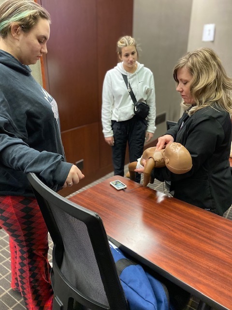 nurse showing two female students how to perform cpr on an infant