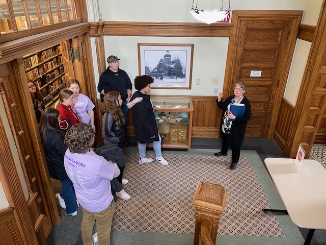 students listening to their tour guide from the library at the bottom of the staircase