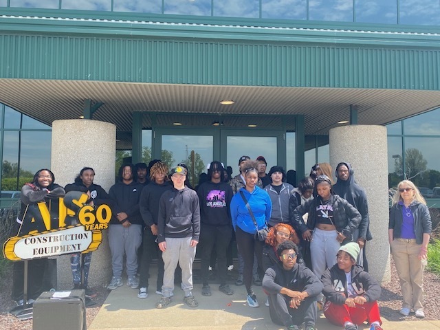 Group of students outside the AIS Equipment Building with the AIS logo and sign