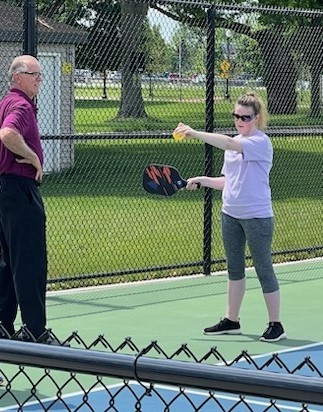 Student with a seeing disability getting read to serve in pickleball with an instructor at her side