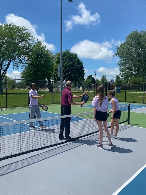 Four students and an instructor on a pickleball court lwith rackets learning how to play pickleball
