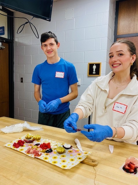 One male and one female student with huge smiles putting together a cheese board