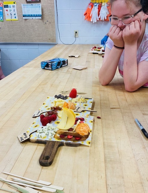 female student smiling with her hands to her face admiring her chesse and fruit board