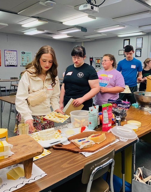 four students in line choosing different types of cheeses to sample