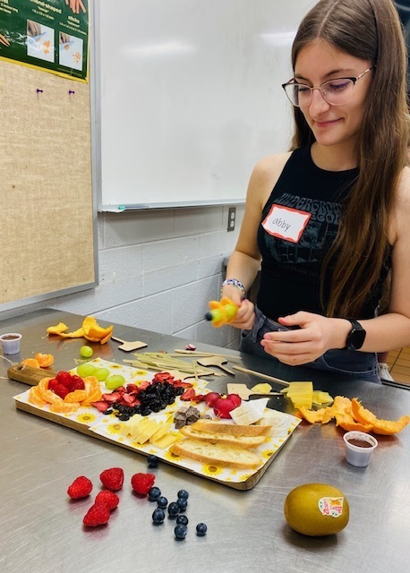 female student putting fruit kabobs together