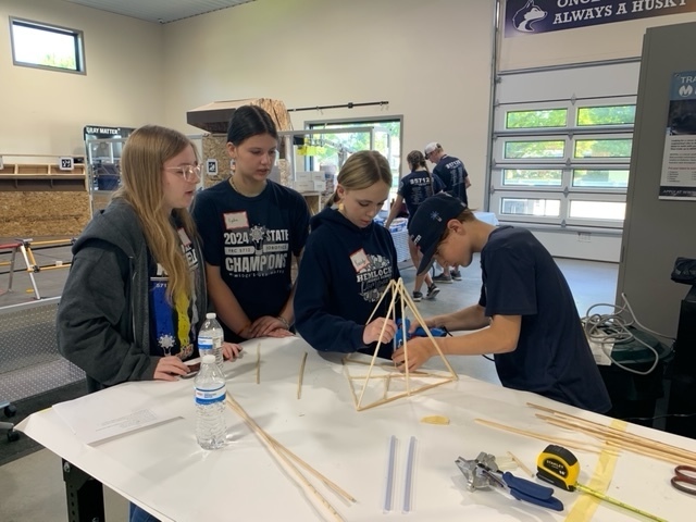 Four students making  a tower structure out of sticks and glue guns. 