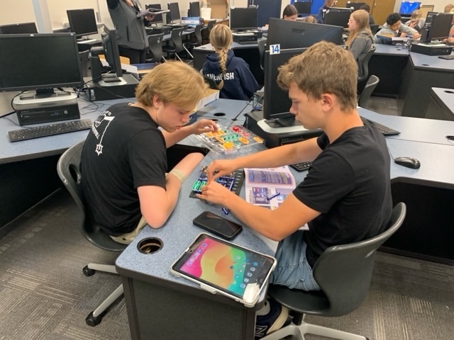 Two students working on the insides of a computer  at a computer desk  