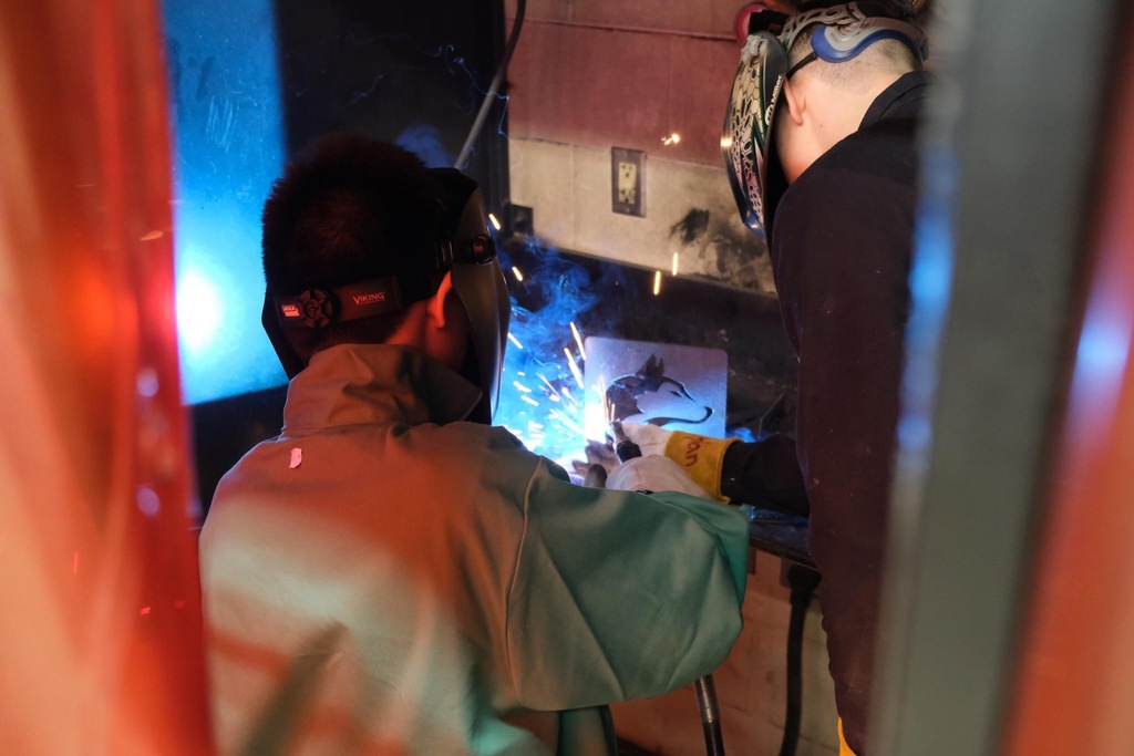 Back view of a student who is welding and lighting sparks from the weld