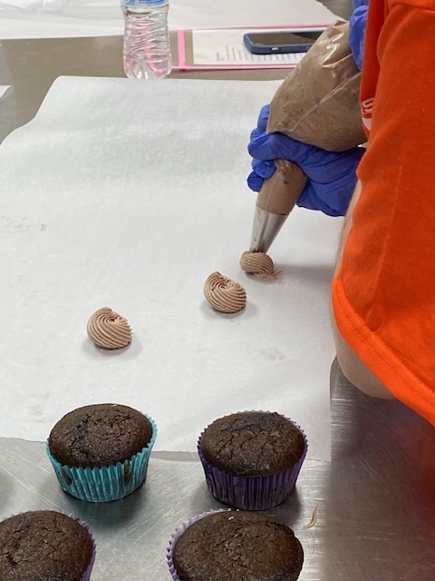 chocolate frosting being placed on parchment paper through a frosting bag