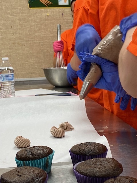 Students with piping bags in their hands putting frosting on parchment paper