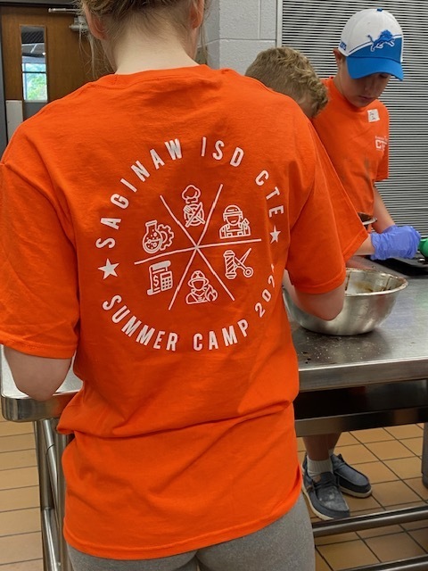 Back of a camper's tee shirt that says Saginaw ISD CTE Summer Camp 2024 with five graphics highlighting firefighting, culinary, STEM, barbershop, accounting, and military