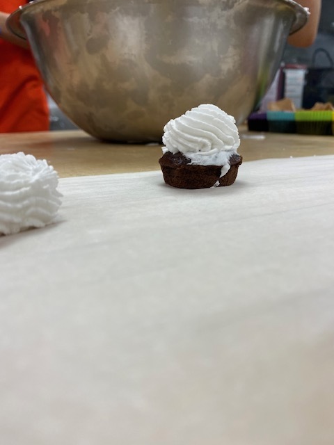 chocolate cupcake with white frosting sitting in front of a stainless steel mixing bowl