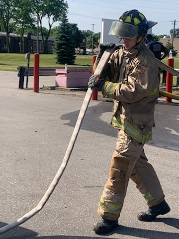 Student firefighter rolling up a fire hose in full gear