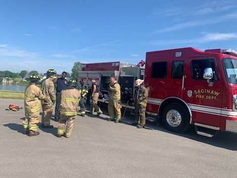 Students in full fire fighter gear and saginaw fire department fire fighters in front of a red engine truck