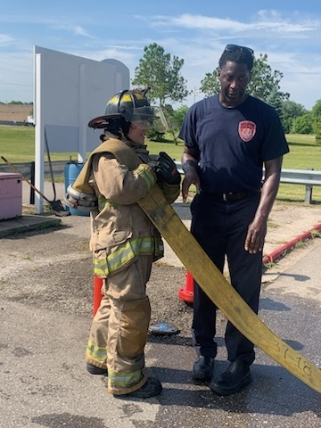 Student holding a fire hose that is unoperational with an adult firefighter looking on