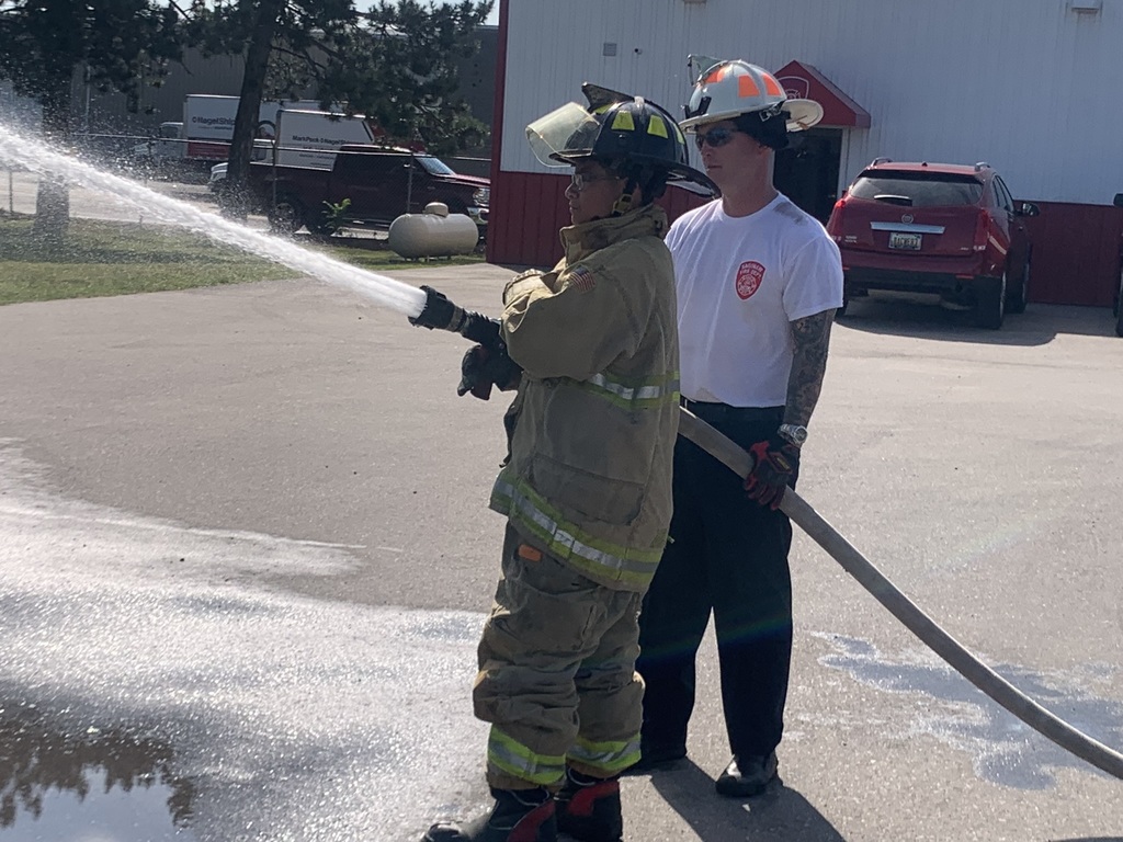 Saginaw City Firefighter with student holding a hose with water coming out