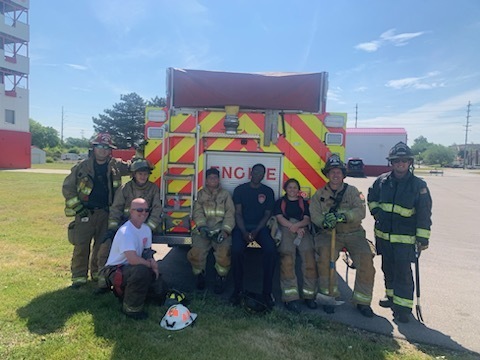 Saginhaw Fire Department Firefighters and students sitting and standing in front of a fire engine outdoors in full gear