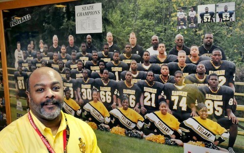 Coach Durrett poses in front of picture of high school football team