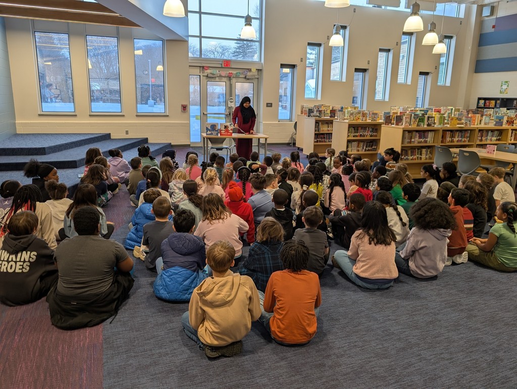 woman wearing a hijab standing behind a table speaking to a group of students