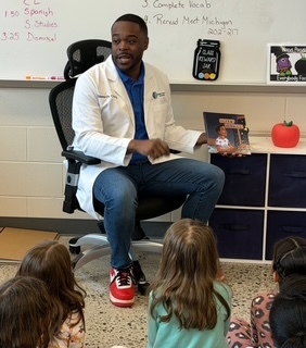 doctor holding children's book he wrote in front of a class