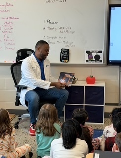 a dr holding a book sitting in chair in front of class 