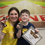 student holding award & pine wood derby car w/ certificate. W/ an adult