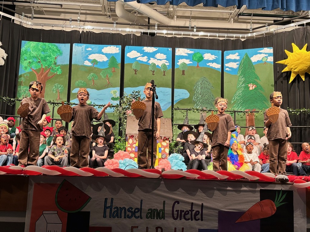 5 students standing on stage. holding large paper acorns