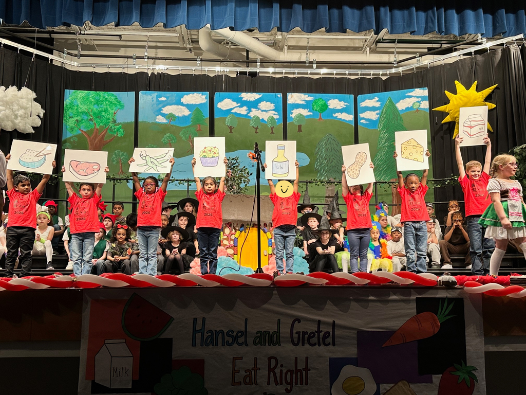 students on stage. 8 standing wearing red shirts holding signs with food on them