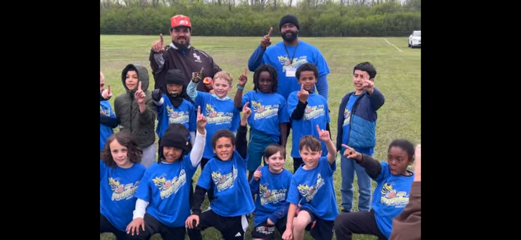 13 children holding up their pointer finger for #1 with 2 ocaches also holding the #1 finger up
