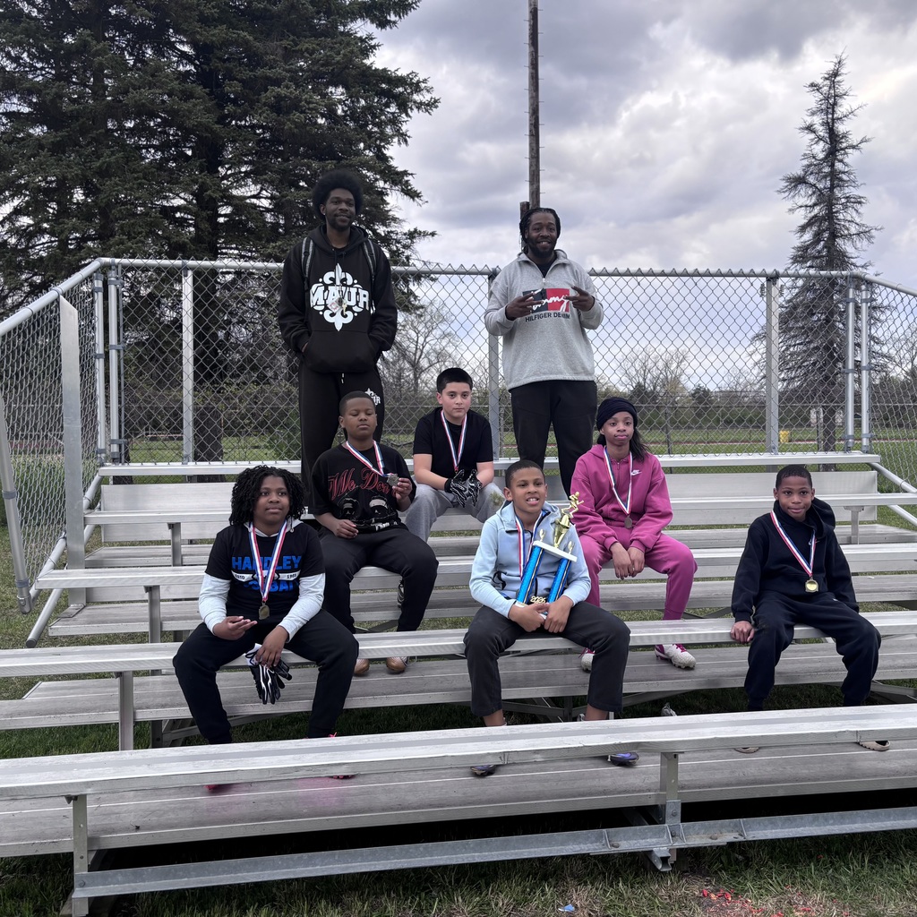 6 students sitting on bleachers wearing medals & 1 holding a trophy. 2 coaches standing in the back. (students have varying ethnicties.)