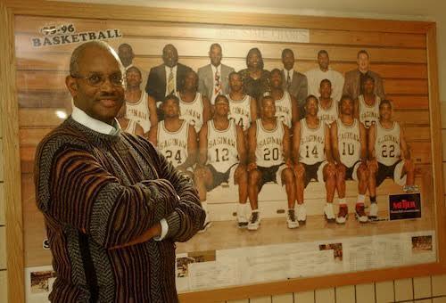 Coach T stands in front of picture of basketball team