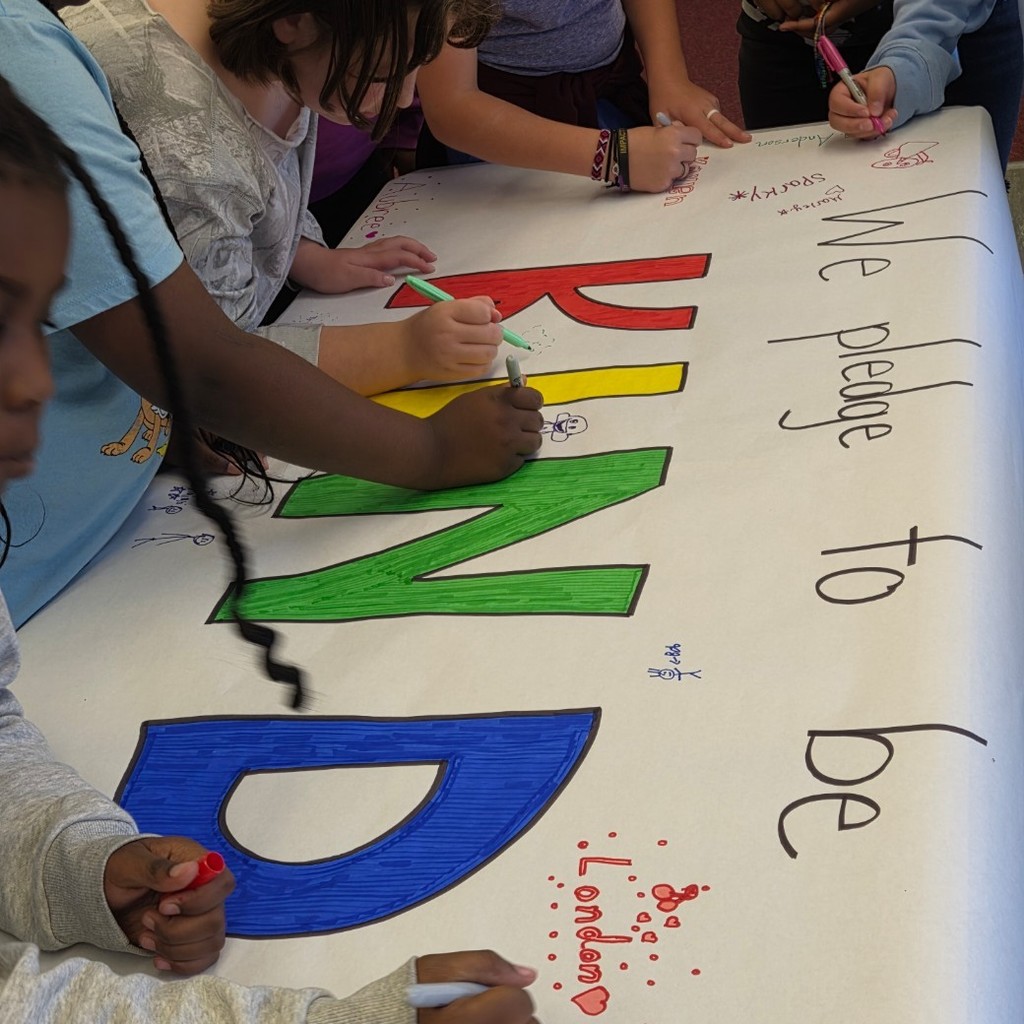 students sign banner that reads "we pledge to be kind"