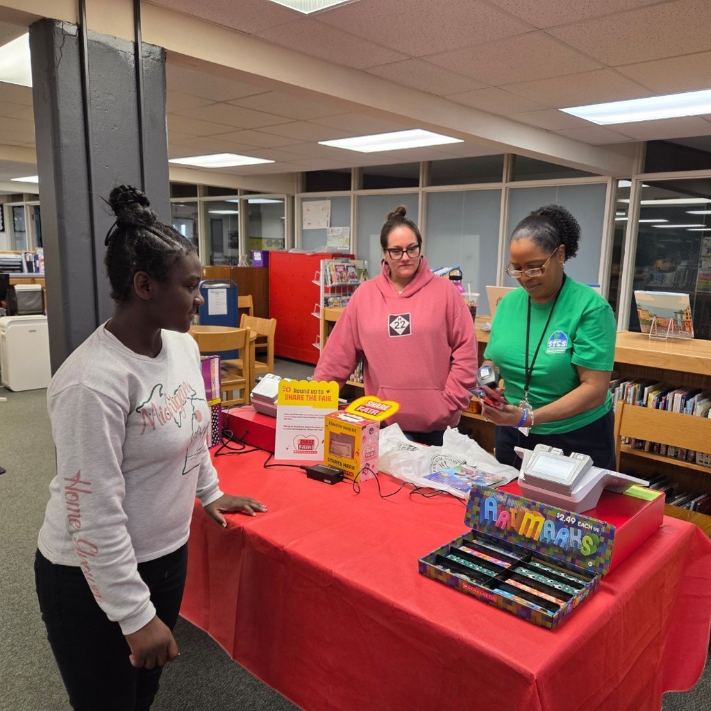 Ms. Charity and a parent volunteer check out a book for a student