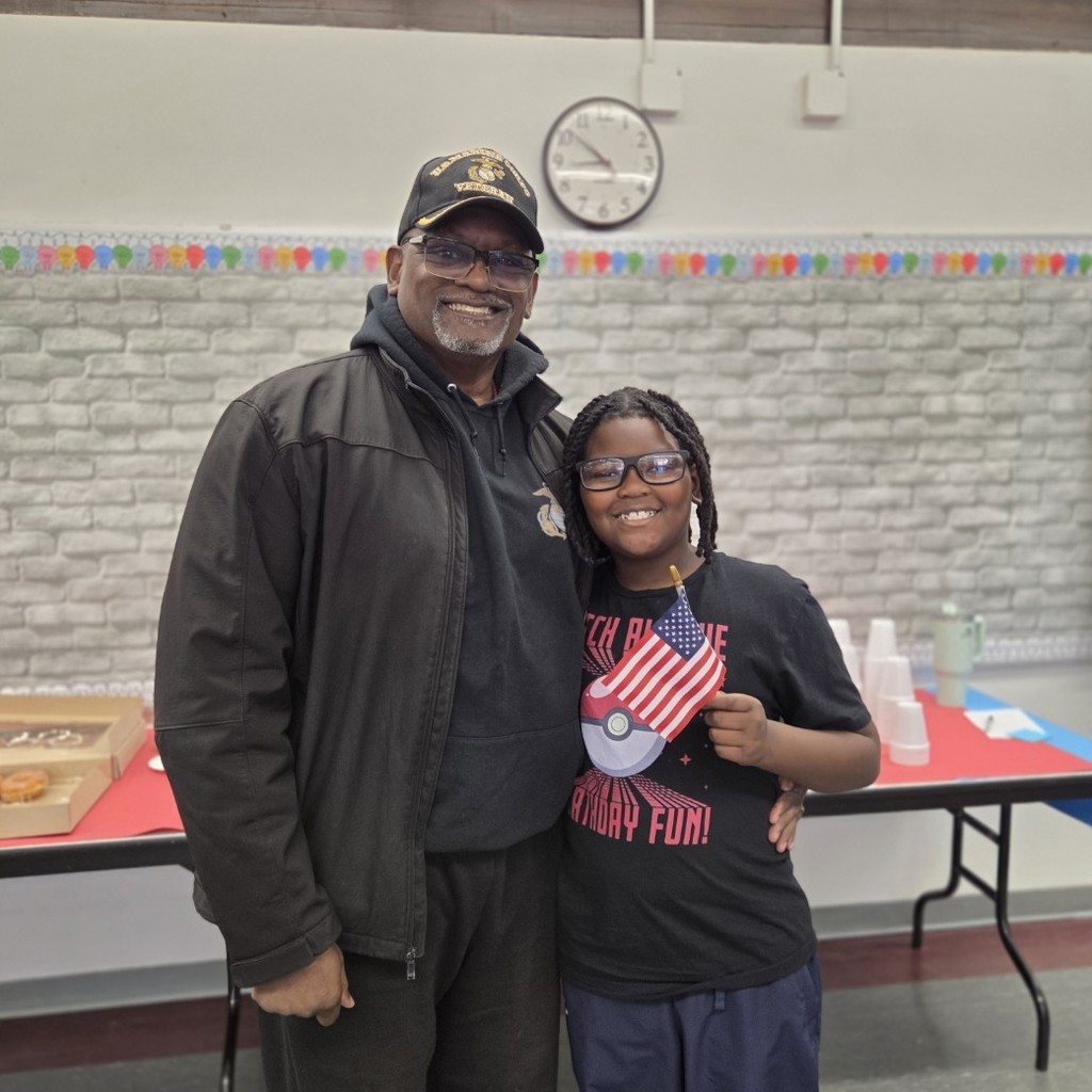 student stands with veteran guest and holds flag