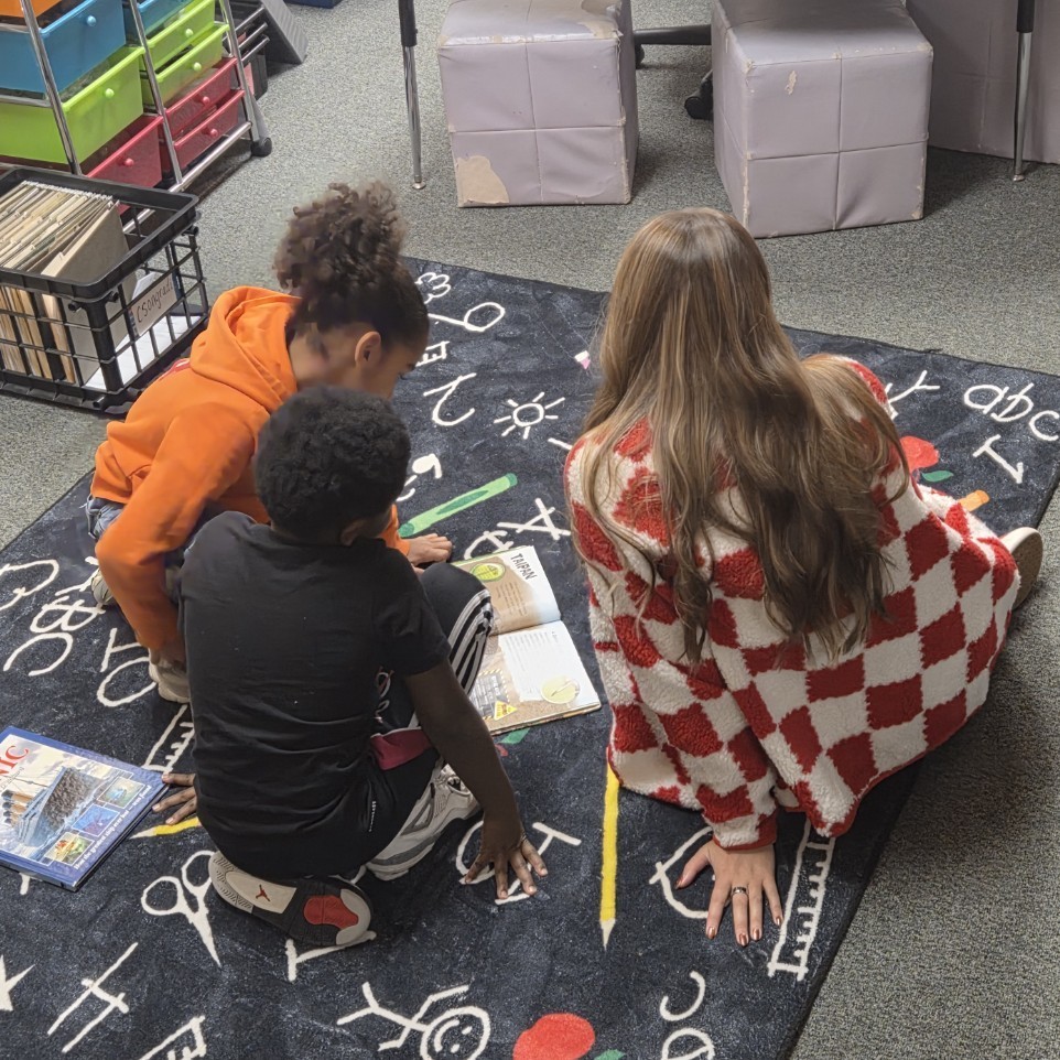 teacher reads with 2 students at carpet